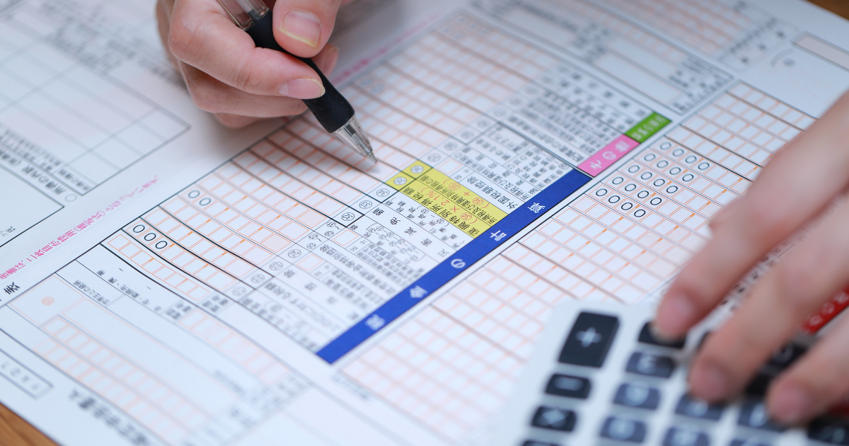 確定申告書にペンで記入している手元と電卓のアップ
