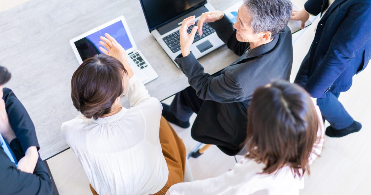 パソコンや資料を囲んで会議をするビジネスパーソンたち