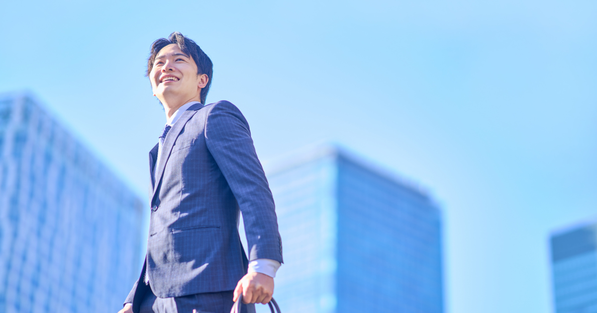 青空を背景に笑顔で歩くスーツ姿の男性