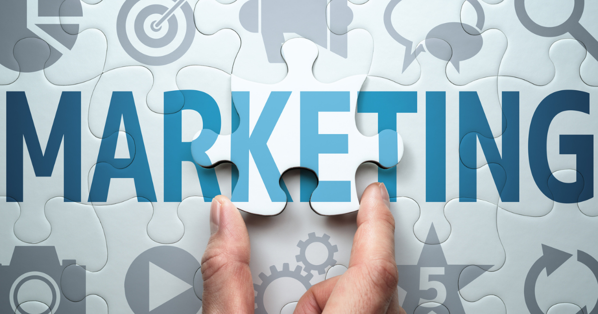 「MARKETING」という文字が書かれたパズルの最後のピースをはめようとしている手