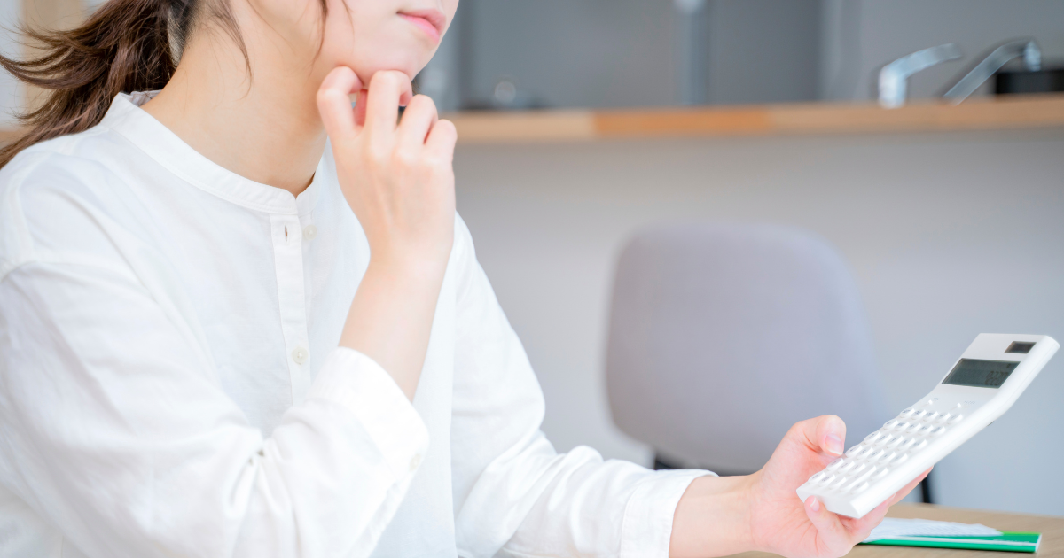 電卓を持ちながら顎に手を当てて悩む女性