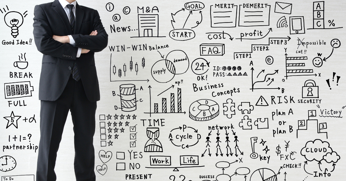 ビジネス関連の図解が描かれたホワイトボードの前に立つ、腕組みをしたスーツ姿の男性