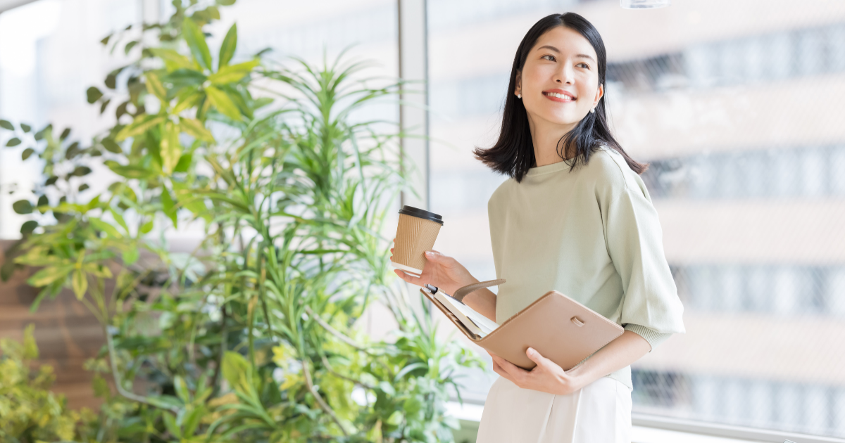 コーヒーカップとバインダーを持って笑顔で立つ女性